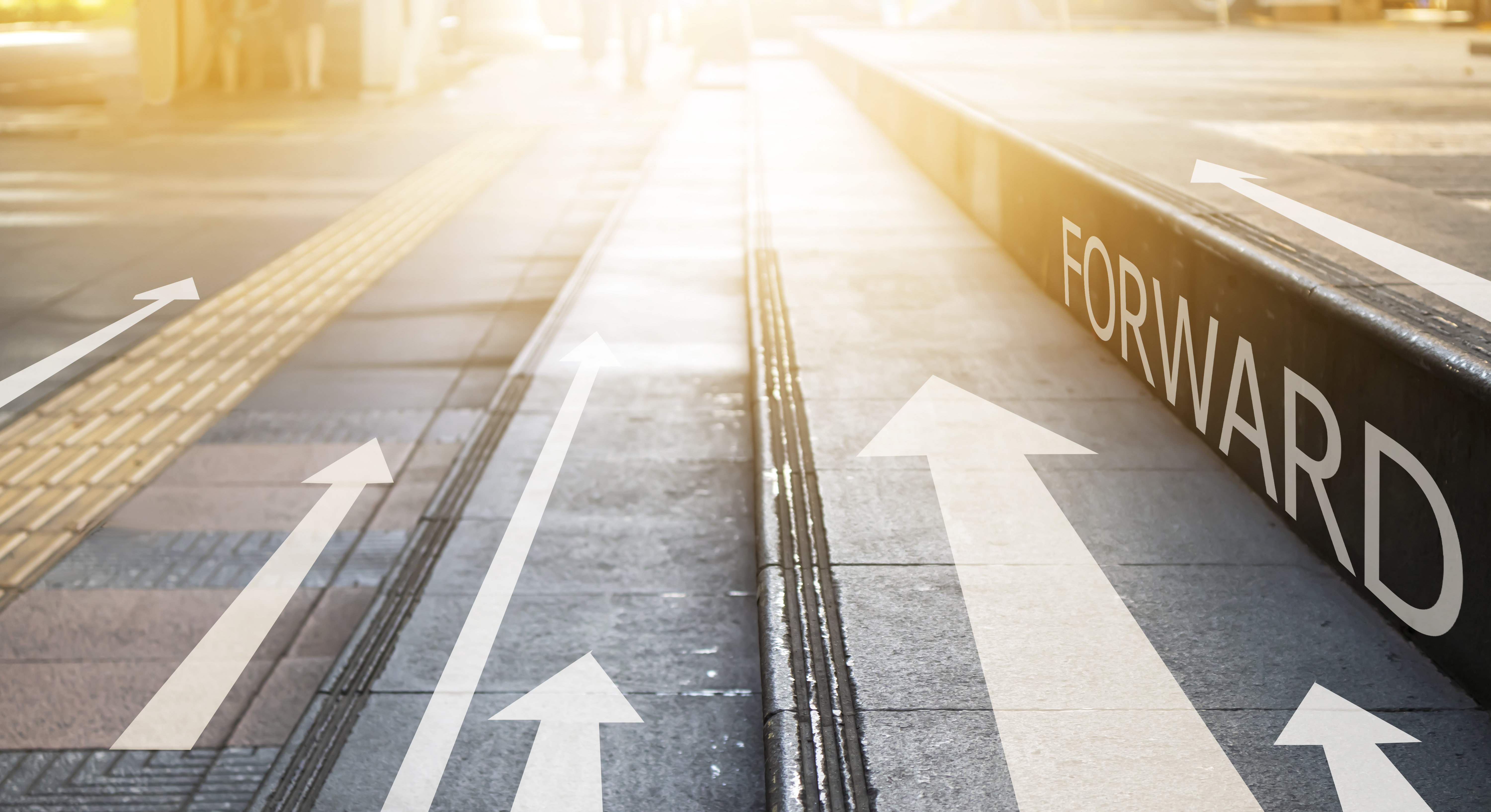 A picture of tram tracks with white arrows all pointing towards the horizon and the word forward written in white text on the platform edge