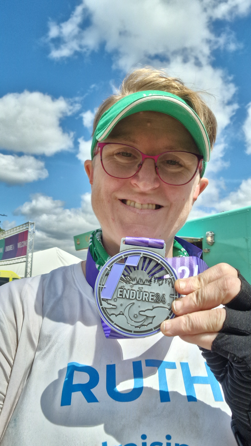 Photo of Ruth holding her medal to the camera, which says Endure24 on it.