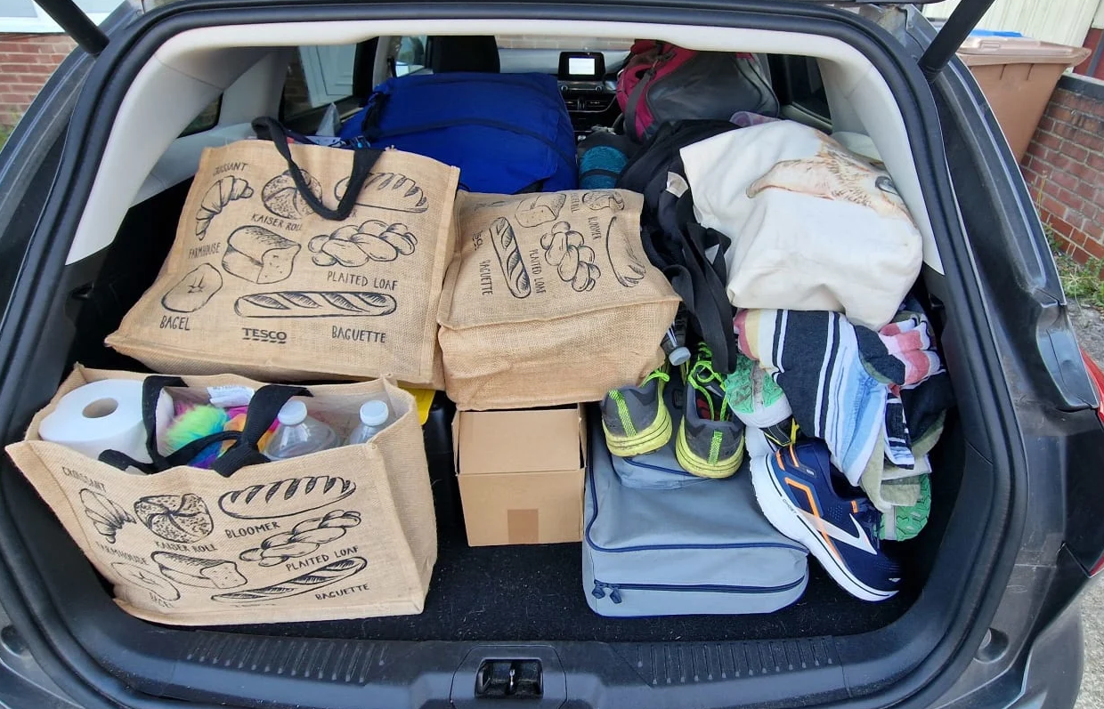 A photo of a car boot loaded up with lots of bags, trainers and a large tent