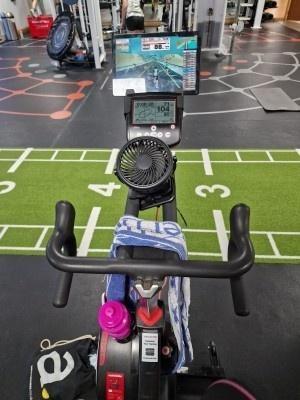 a photo of a bike in the gym attached to Zwift on a tablet with a fan clipped to the handlebars