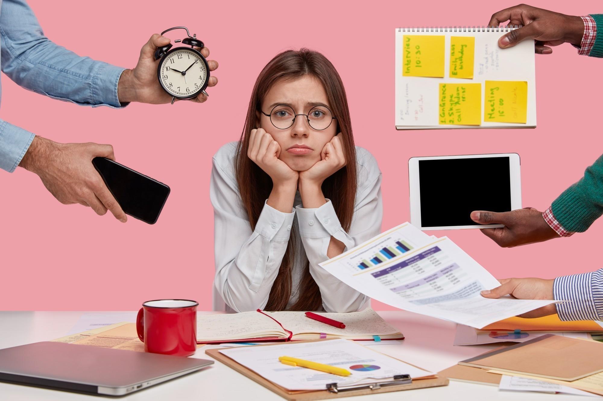 A photo of a sad looking woman with long dark hair surrounded by arms held at her with things she hasn't done, and a desk full of work.