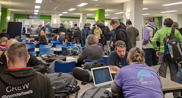 Photo of a cafe with lots of tables that have people with laptops working and a long queue for the counter.