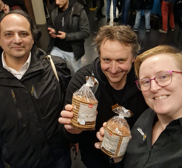 A photo of three people standing together, two on the right are holding stroopwafell and they are all smiling at the camera.