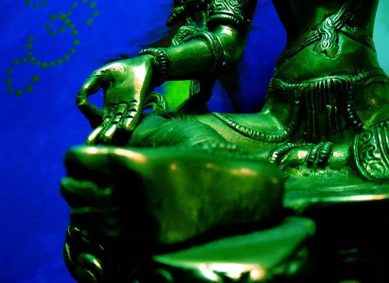 A photo of a Green Tara rupa with her foot close to the camera in focus, stepping out into the world, and her hand on her knee with the thumb and first finger touching.