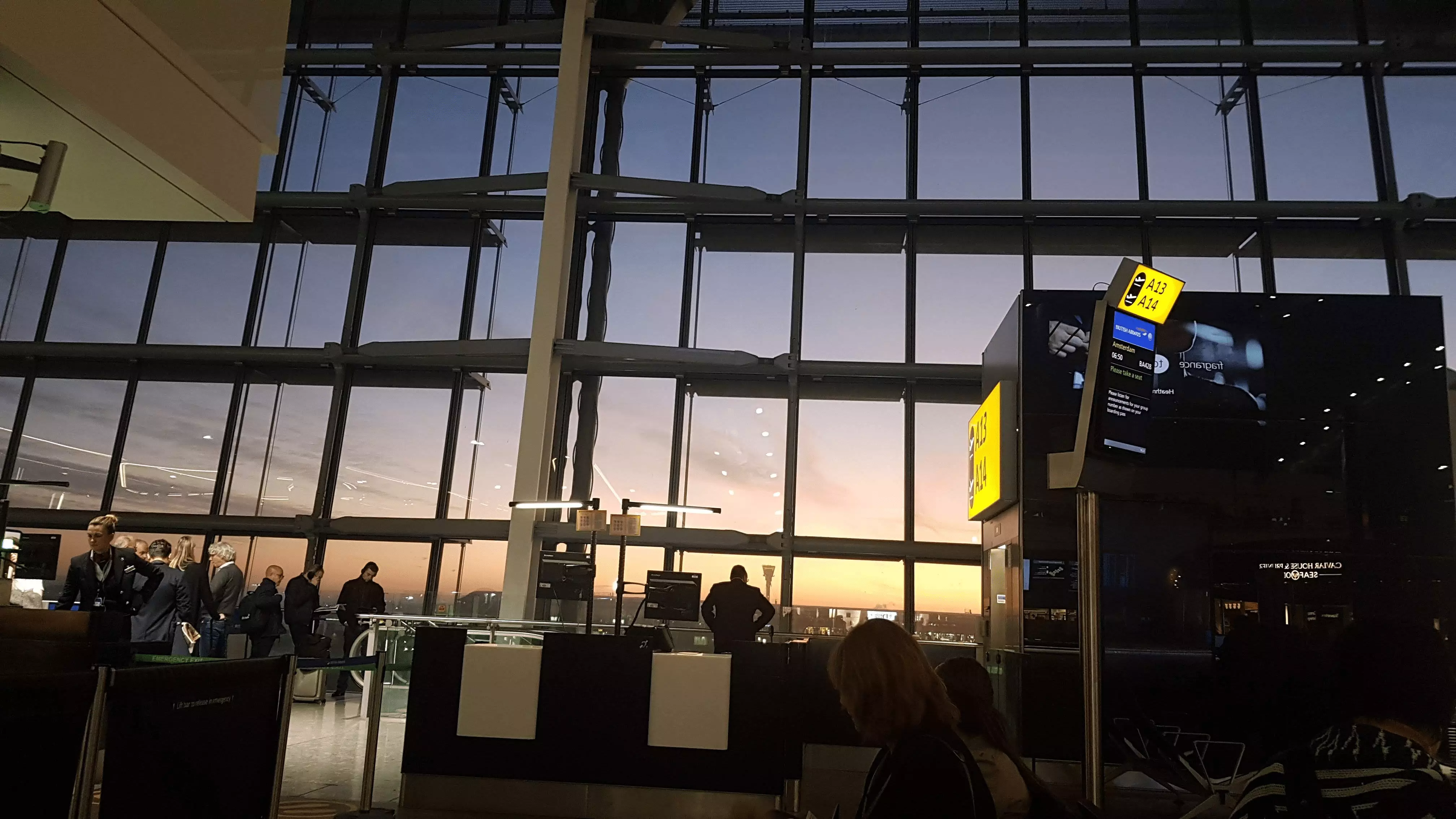 Photo of Heathrow airport with the sun setting over the horizon looking through large glass windows.