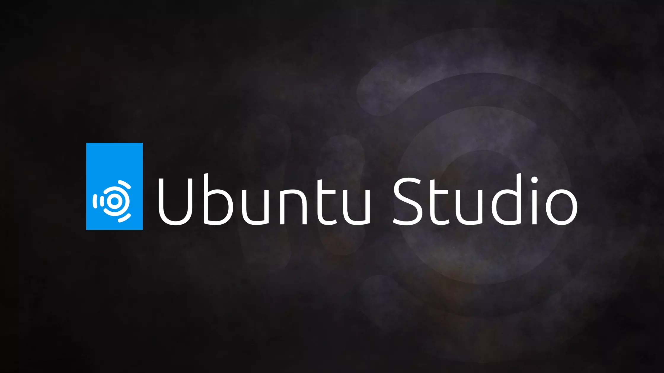 Ubuntu studio logo on the dark wallpaper which is black with a mottled grey image of the ubuntu studio logo on the right side - a circle with several concentric circles outside it.