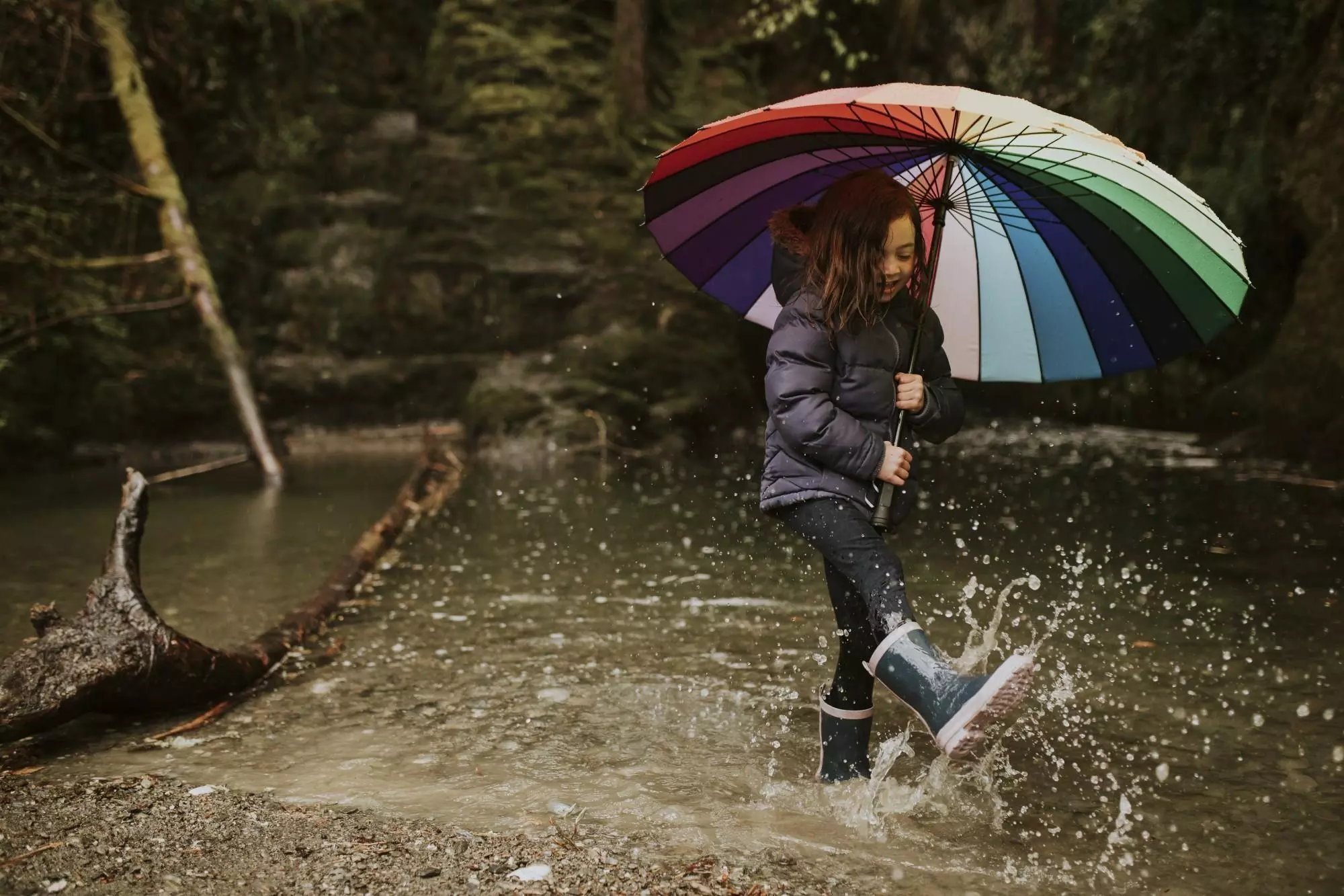 A happy girl playing by the forest lake with an umbrella on a rainy day